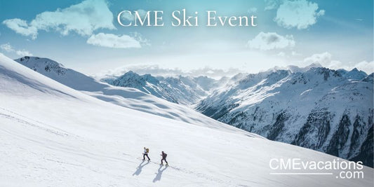 Two people skiing down a snow-covered mountain with a scenic view of the snowy landscape and mountains in the background.