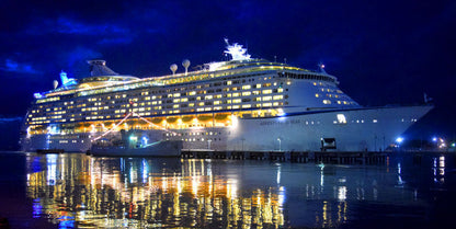 Cruise ship at night with blue and yellow lights reflecting on water