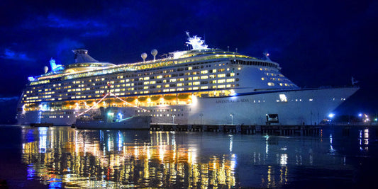 Cruise ship at night with blue and yellow lights reflecting on water
