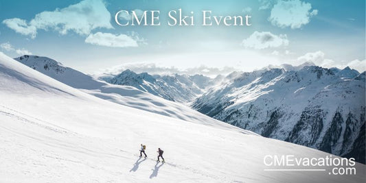 Two people skiing down a snow-covered mountain with a scenic view of the snowy landscape and mountains in the background.