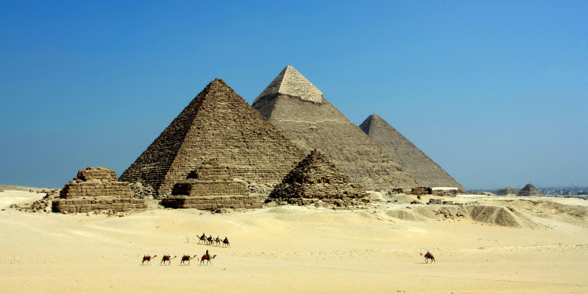 Pyramids of Giza with camels in the foreground under a clear blue sky
