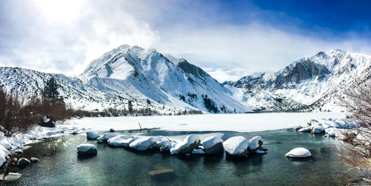 Snow-covered mountains and a frozen lake with rocks in the foreground.